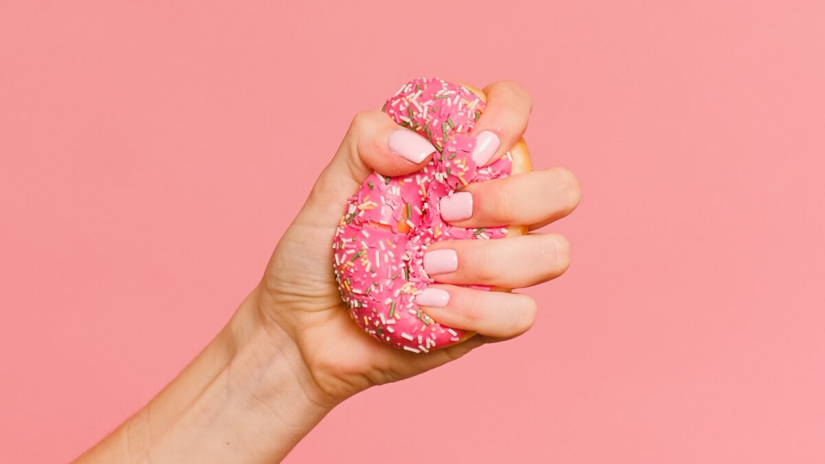 A hand crushing a pink iced doughnut