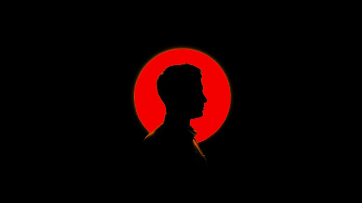 Side profile silhouette of a man's head and shoulders in front of a red light